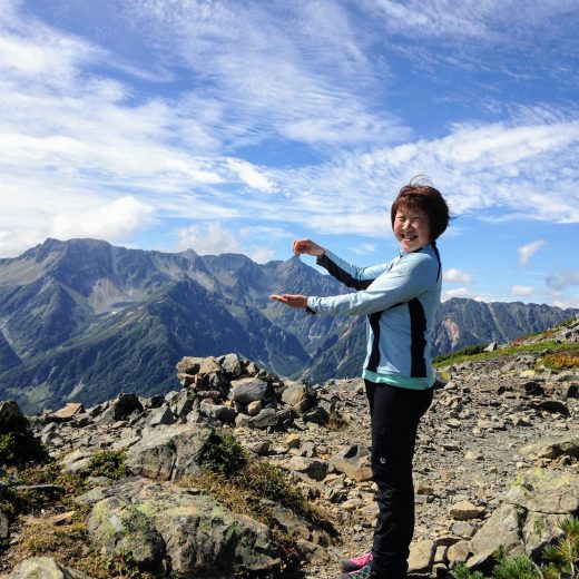 遠近法で、奥にある山の先端を掴んでいるようなポーズをしている阪本朱水子さんの写真