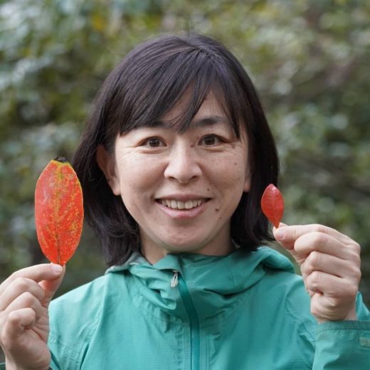 大小のオレンジ色の葉っぱを両手に持った水野 由香さんが微笑んでいる写真