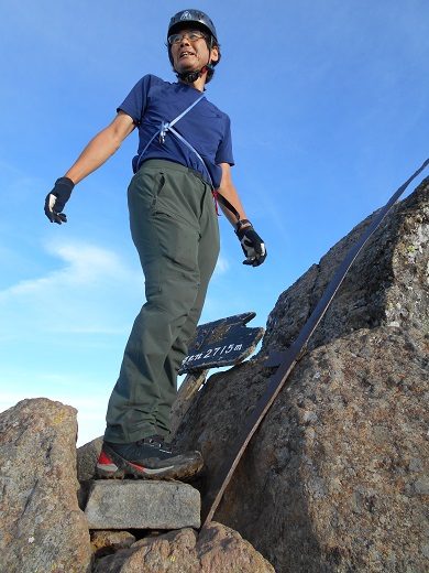 青空の下、山頂にある岩の上に立ち、遠くを眺めている西埜 義紀さんの写真